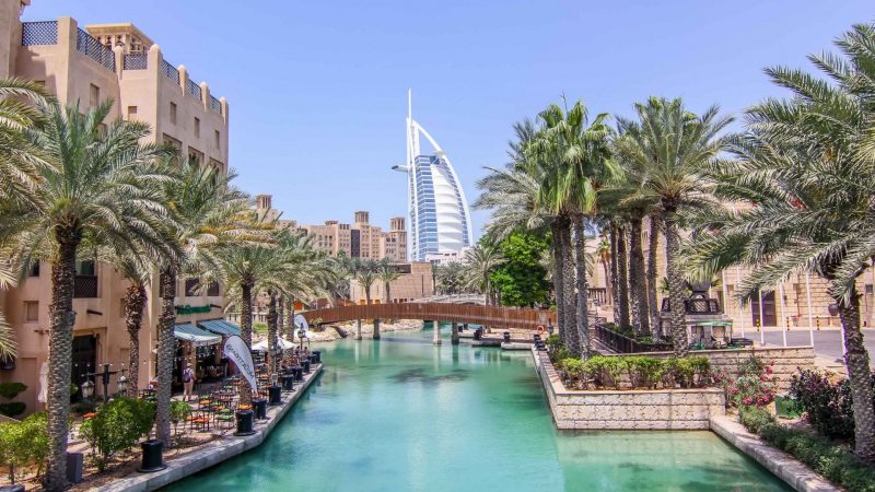 Madinat Jumeirah'nın geleneksel mimarisi, palmiye ağaçları ve kanalın arkasında yükselen Burj Al Arab manzarası; kültürel bir dubai şehir turu.
