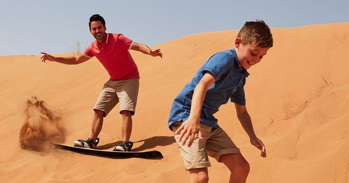 Dubai çöl safarisinde kum tepelerinde sandboarding yapan iki çocuk