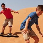 Dubai çöl safarisinde kum tepelerinde sandboarding yapan iki çocuk