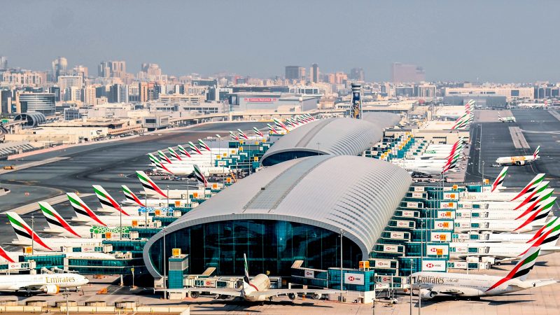 Çok sayıda Fly Dubai ve Emirates uçağının park halinde olduğu, arka planda şehir silüetinin görüldüğü Dubai Uluslararası Havalimanı'nın kuş bakışı görünümü.